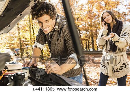 Stock Photography - Man looking in car bonnet, woman on cell phone. Fotosearch