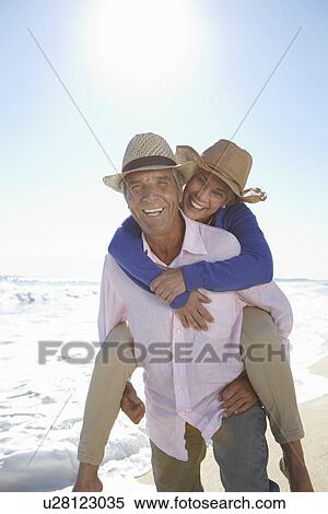 Stock Photography - Man piggy-backing woman on beach. Fotosearch