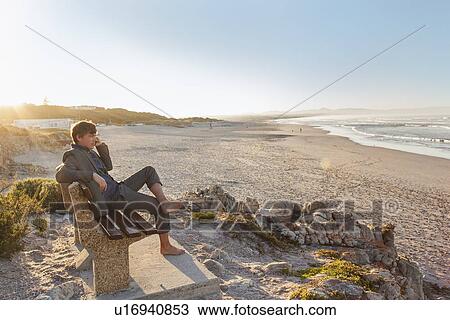 Stock Image - Man relaxing on beach bench. Fotosearch