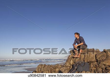 Man sitting on rock at seaside View Large Photo Image Stock Image - Man sitting on rock at seaside. Fotosearch