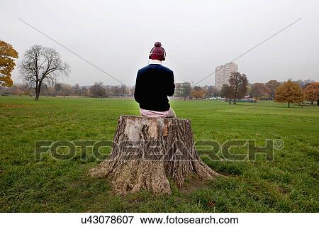 Stock Photo - Man sitting on tree stump listening to music. Fotosearch