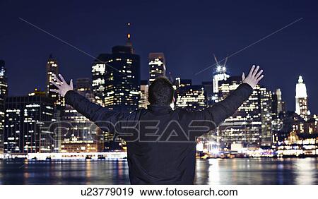 Stock Photo - Man with arms outstretched at night, New York City, USA. Fotosearch