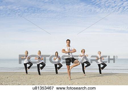 Stock Photo - Mature and senior women and trainer practicing tree pose on beach. Fotosearch