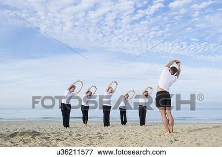 Stock Photo - Mature and senior women with their trainer exercising on beach. Fotosearch