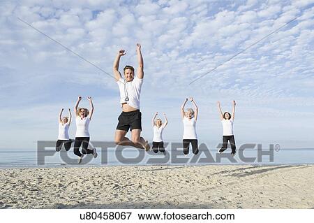 Stock Photo - Mature and senior women with their trainer jumping on beach. Fotosearch
