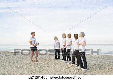 Stock Photography - Mature and senior women with their trainer on beach. Fotosearch