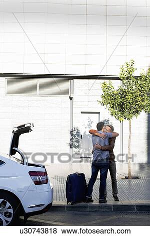 Mature male couple hugging next to car and suitcase View Large Photo Image Stock Photo - Mature male couple hugging next to car and suitcase. Fotosearch