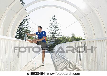 Mature male runner stretching leg on footbridge View Large Photo Image Picture - Mature male runner stretching leg on footbridge. Fotosearch