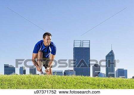 Stock Image - Mature male runner tying shoelaces, Perth, Australia. Fotosearch