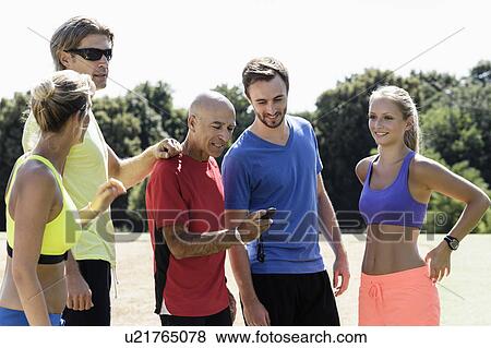 Stock Photo - Mature male trainer and a group of adult runners looking at stopwatch. Fotosearch