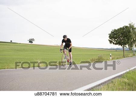 Stock Image - Mature man cycling along country road. Fotosearch