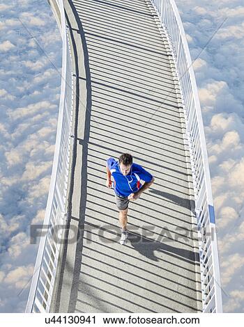 Stock Image - Mature man running on curved footbridge above the clouds. Fotosearch