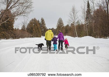 Stock Image - Mother and father with two children and dog, walking in snow, rear view. Fotosearch