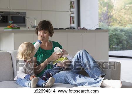 Picture - Mother, baby boy and female toddler sitting on sofa. Fotosearch