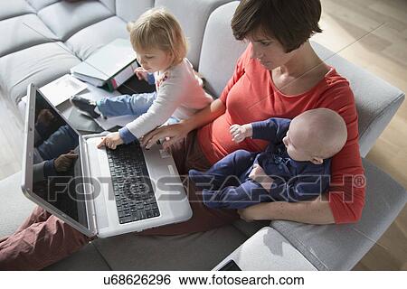 Mother, baby boy and female toddler using laptop on sofa View Large Photo Image Stock Photograph - Mother, baby boy and female toddler using laptop on sofa. Fotosearch