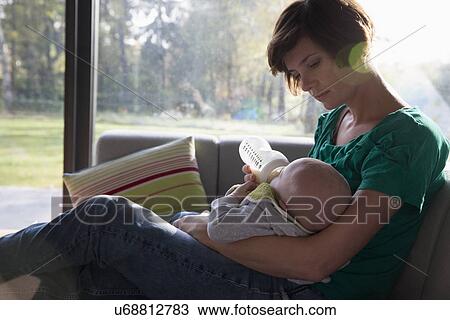 Mother feeding bottle to baby boy on sofa View Large Photo Image Stock Image - Mother feeding bottle to baby boy on sofa. Fotosearch