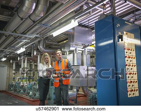 Stock Image - Office workers using digital tablet and camera to check efficiency of office heating in boiler room. Fotosearch