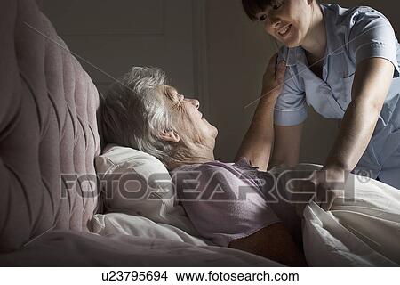 Picture - Personal care assistant chatting to senior woman in bed. Fotosearch