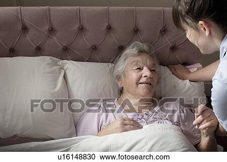 Stock Image - Personal care assistant chatting to senior woman in bed. Fotosearch