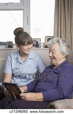 Stock Image - Personal care assistant looking at photograph with senior woman. Fotosearch