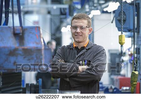 Stock Photo - Portrait of engineering apprentice in engineering factory, smiling. Fotosearch