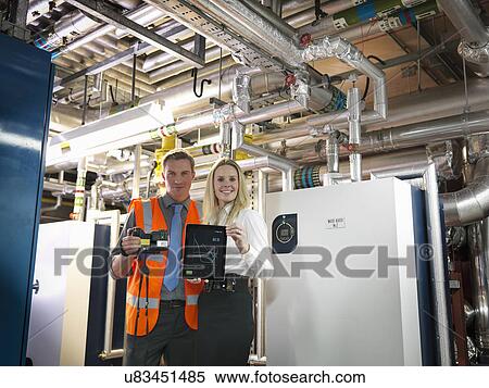 Stock Photography - Portrait of office workers using digital tablet and camera to check efficiency of office heating in boiler room. Fotosearch
