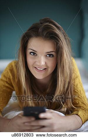 Stock Image - Portrait of teenage girl in bedroom with smartphone. Fotosearch