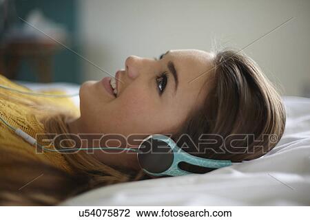 Portrait of teenage girl lying on bed listening to headphones View Large Photo Image Stock Image - Portrait of teenage girl lying on bed listening to headphones. Fotosearch
