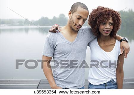 Picture - Portrait of young couple by lake with arms around each other. Fotosearch