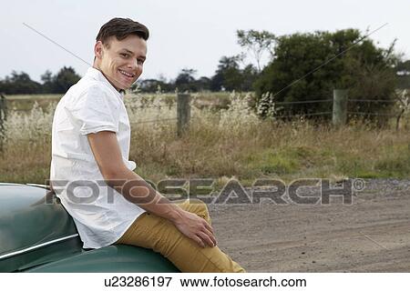 Stock Photo - Portrait of young man sitting on bonnet of vintage morris minor. Fotosearch