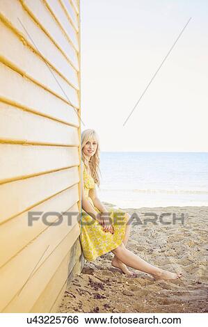 Stock Photograph - Portrait of young woman sitting next to beach huts. Fotosearch
