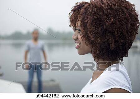 Portrait of young woman smiling with man in background View Large Photo Image Stock Image - Portrait of young woman smiling with man in background. Fotosearch