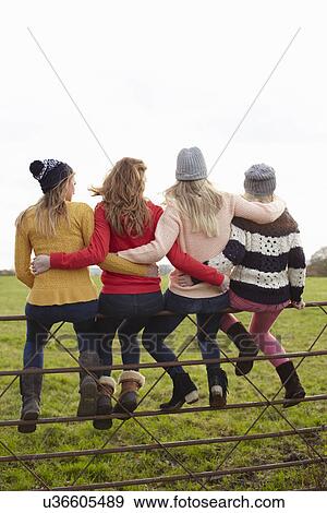 Stock Photo - Rear view of four teenage girls sitting on gate. Fotosearch