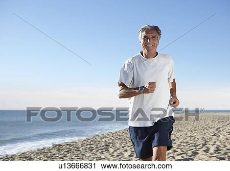 Stock Image - Senior man jogging on beach. Fotosearch