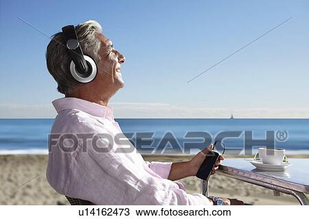 Senior man listening to music with headphones on beach View Large Photo Image Stock Image - Senior man listening to music with headphones on beach. Fotosearch