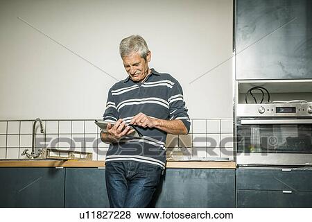 Senior man using digital tablet in kitchen View Large Photo Image Stock Photo - Senior man using digital tablet in kitchen. Fotosearch