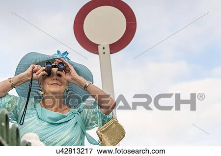 Stock Photo - Senior woman at races looking through binoculars. Fotosearch