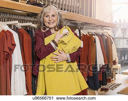 Stock Image - Senior woman holding dress in boutique. Fotosearch