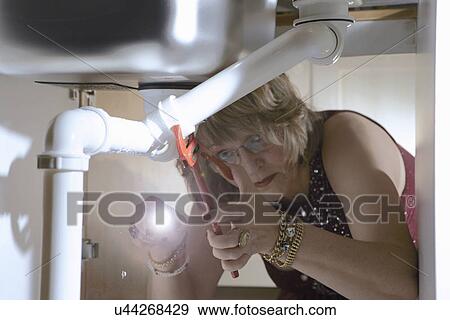 Senior woman in evening wear fixing pipes under kitchen sink View Large Photo Image Stock Photo - Senior woman in evening wear fixing pipes under kitchen sink. Fotosearch