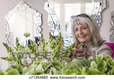 Stock Image - Senior woman looking at flowers in florist shop. Fotosearch