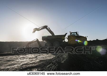 Stock Photography - Silhouette of digger and dumper truck loading coal in surface coal mine. Fotosearch