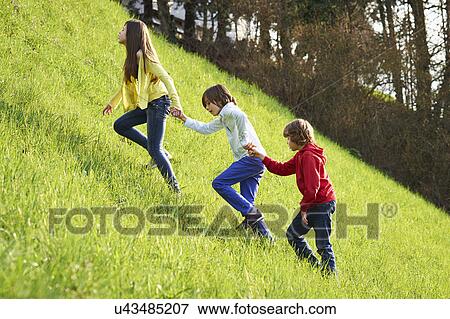 Sister and younger brothers climbing up grassy field View Large Photo Image Stock Photo - Sister and younger brothers climbing up grassy field. Fotosearch