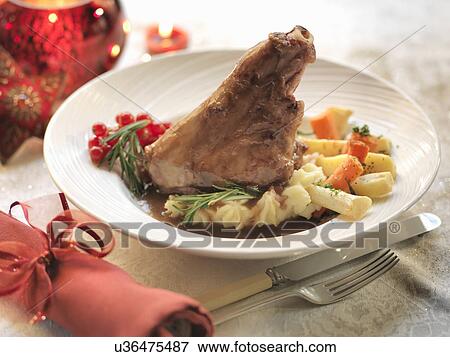 Stock Photo - Slow cooked lamb shank with fresh rosemary, carrots, potatoes, Italian beans, white wine and garlic among festive decorations. Fotosearch