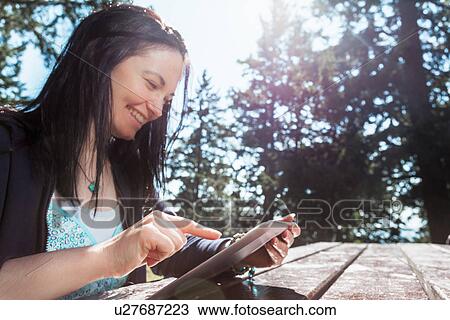 Smiling mature woman using digital tablet at picnic table View Large Photo Image Stock Image - Smiling mature woman using digital tablet at picnic table. Fotosearch