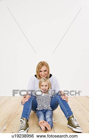 Stock Photograph - Studio portrait of mother and daughter sitting on floor. Fotosearch
