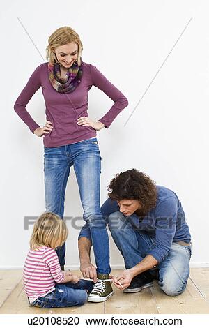 Stock Image - Studio portrait of mother having shoe laces tied. Fotosearch