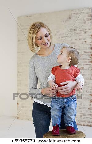 Studio portrait of mother holding baby daughter on stool View Large Photo Image Stock Photo - Studio portrait of mother holding baby daughter on stool. Fotosearch