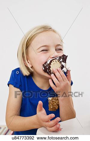 Stock Image - Studio portrait of young girl eating chocolate marshmallow. Fotosearch