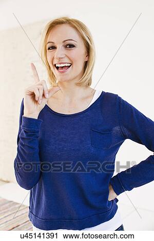 Stock Image - Studio portrait of young woman pointing finger. Fotosearch