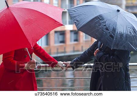 Stock Photograph - Symmetrical couple holding handrail and carrying umbrella's. Fotosearch
